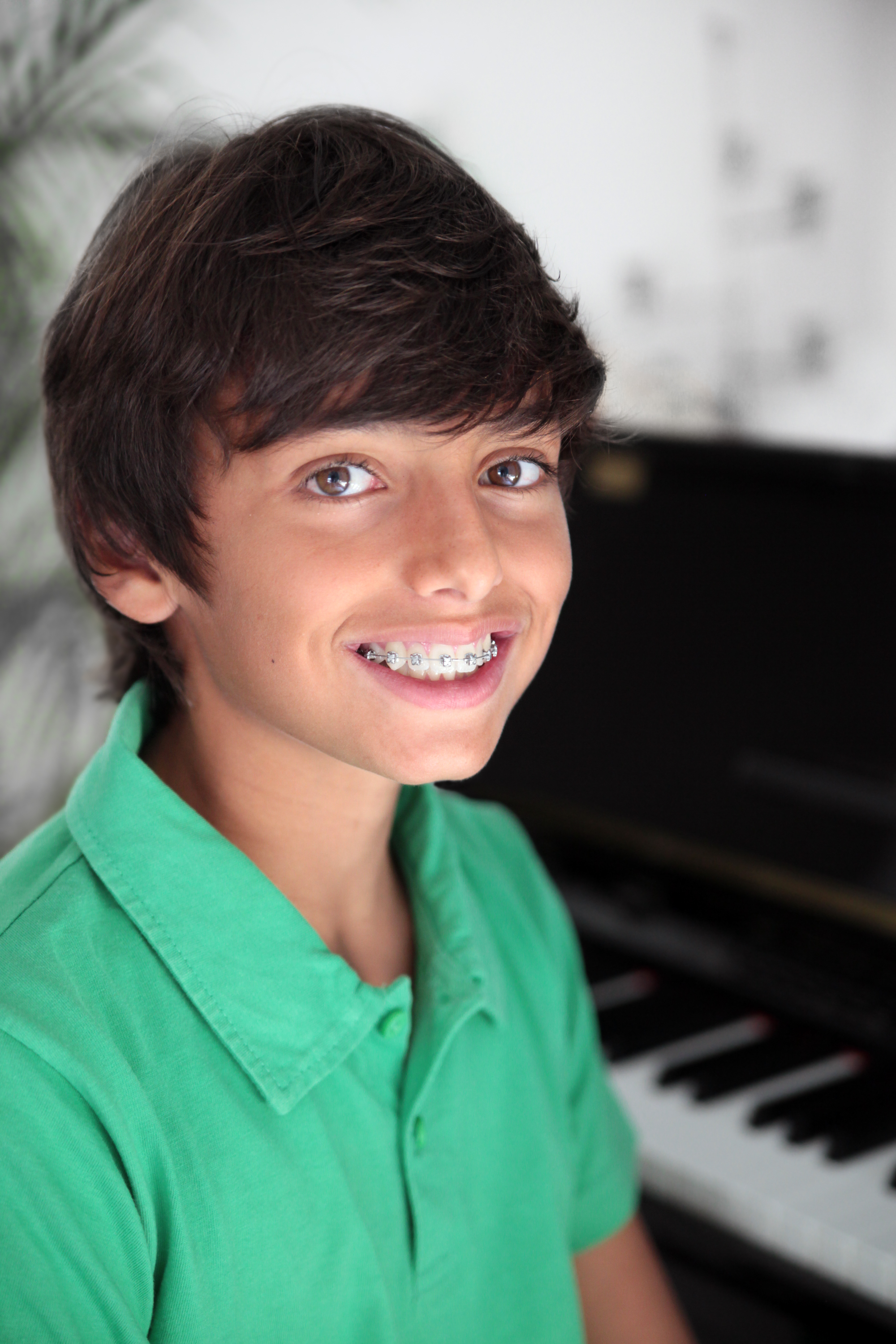 Young boy smiling with braces sitting at a piano